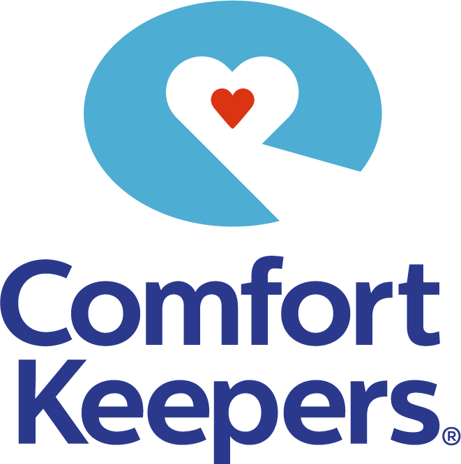 The Comfort Keepers logo features a stylized blue oval with a white hand forming a heart shape that contains a red heart. Below, the words “Comfort Keepers” appear in large blue letters.