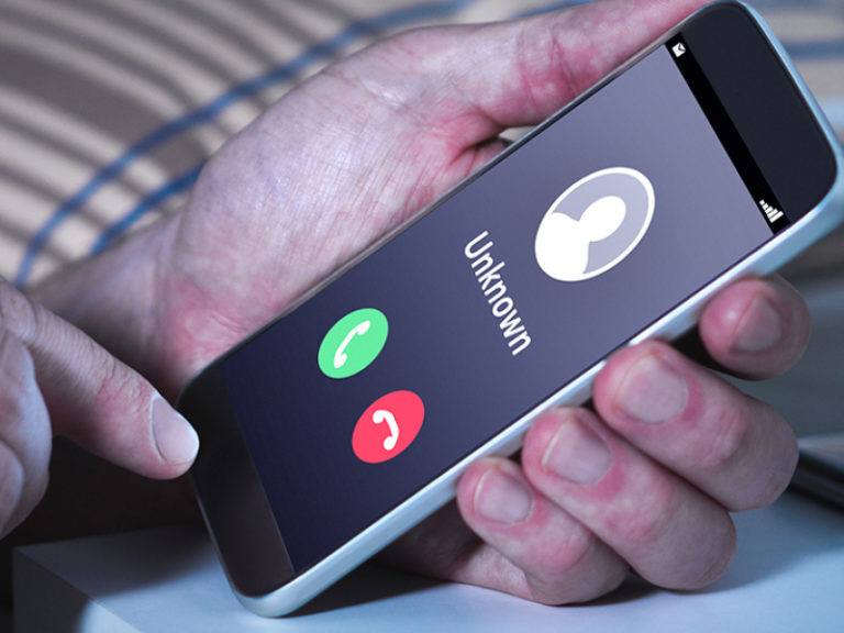 A person holding a smartphone showing an incoming call from an unknown number, with green answer and red decline buttons visible on the screen.