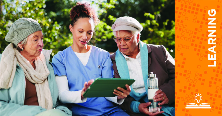 A healthcare worker shows two older women something on a tablet outdoors. All three are seated and engaged. Beside them is an orange graphic with the word LEARNING and an open book icon.