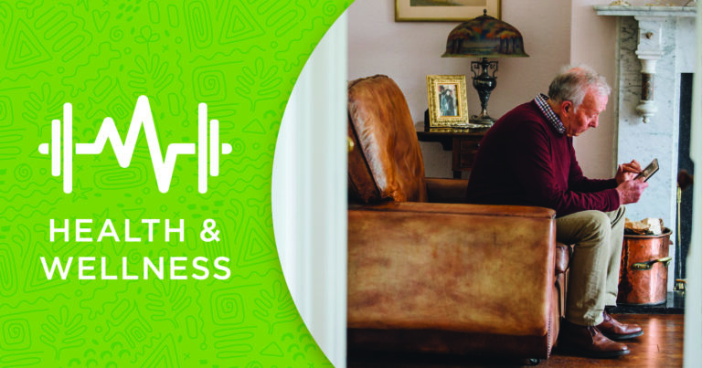 An elderly man sits on a leather chair looking at his phone, next to a fireplace. On the left, a green graphic with a heart and weights reads Health & Wellness.