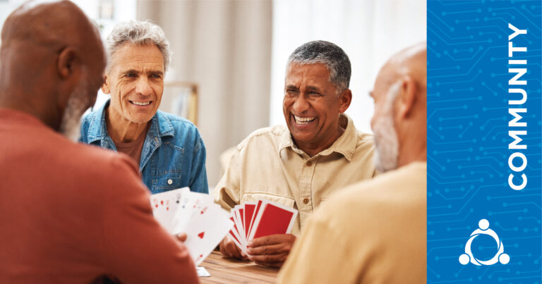 Four older men sit around a table playing cards and smiling. The word COMMUNITY and a graphic are displayed on a blue panel on the right side of the image.