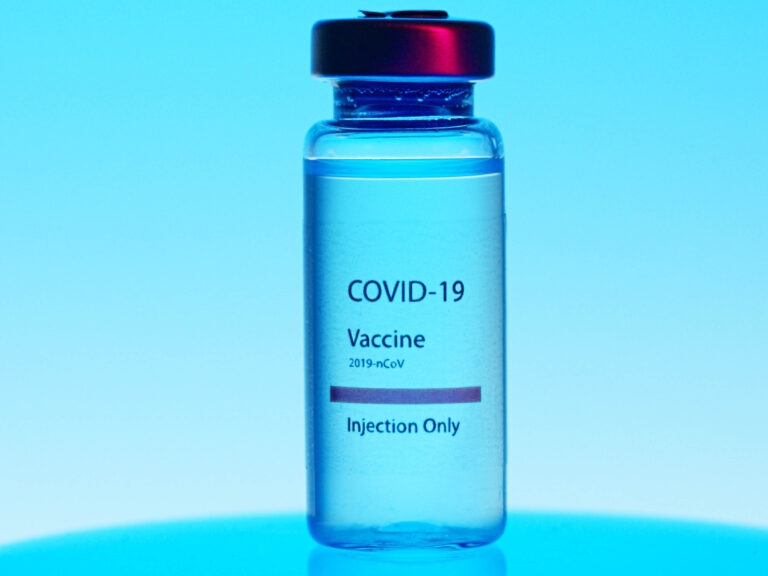 A vial labeled COVID-19 Vaccine 2019-nCoV Injection Only stands upright against a blue background, with a red cap on top.
