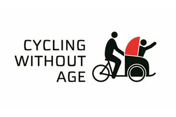 Logo for Cycling Without Age showing a simplified figure pedaling a bicycle with a covered passenger seat at the front, where another figure sits and waves. The text Cycling Without Age appears on the left.