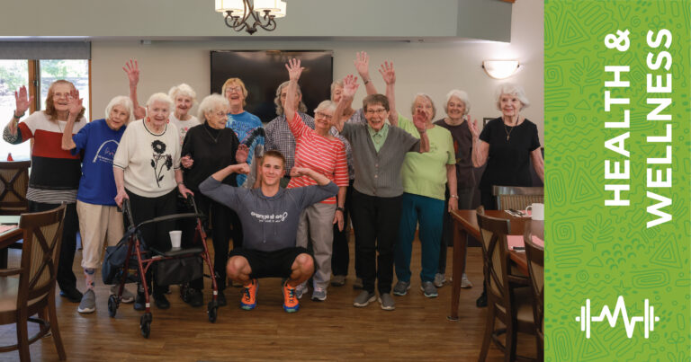 A group of smiling seniors and a young fitness instructor pose together in a room, raising their hands in celebration. A green banner on the right reads Health & Wellness with a heart and dumbbell icon.