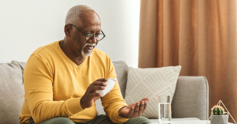 Elderly gentleman looking through his pill box at his supplements and vitamins.