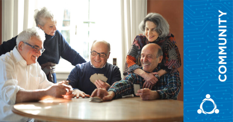 A group of five thankful seniors play cards together at a table, enjoying each other’s company.